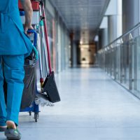 A woman worker in special clothes rolls a trolley for cleaning offices. Cleanroom concept during quarantine. Place for text